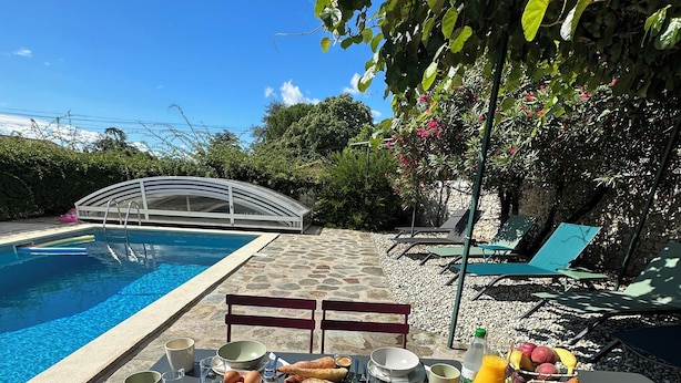 Disposición para comer al aire libre junto a una piscina, con una mesa preparada para el desayuno, incluyendo platos, vasos y una cesta de pan.