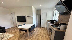 Un espacio habitable compacto con comedor, kitchenette y un televisor de pantalla plana montado en la pared.