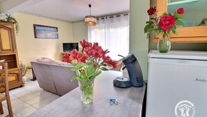 Een woonkamer met een bank, een bijzettafeltje met een bloevas, een televisie en een klok aan de muur.