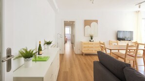 A modern living room with a sofa, a dining area with wooden furniture, a TV, and a hallway leading to another room. - Family Apartment Camp Nou by Maison Piñata (Barcelona)