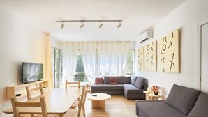 A modern living room with a wooden dining table, chairs, a grey sofa, and a television. - Family Apartment Camp Nou by Maison Piñata (Barcelona)