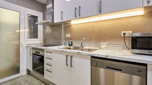 A modern kitchen with white cabinets, stainless steel appliances, and a built-in microwave. - Family Apartment Camp Nou by Maison Piñata (Barcelona)