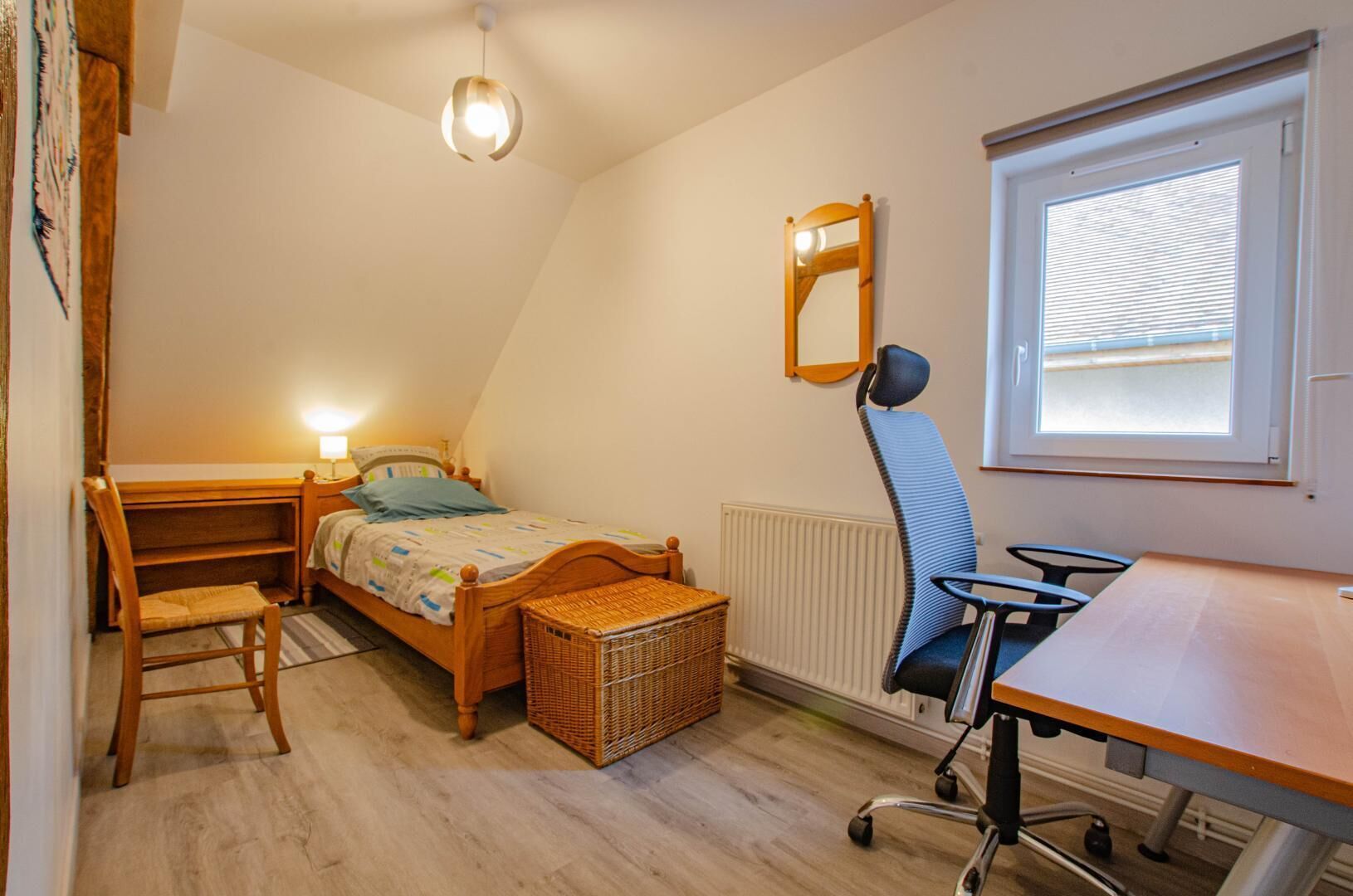 A bedroom with a bed, desk, chair, and a window with blinds.