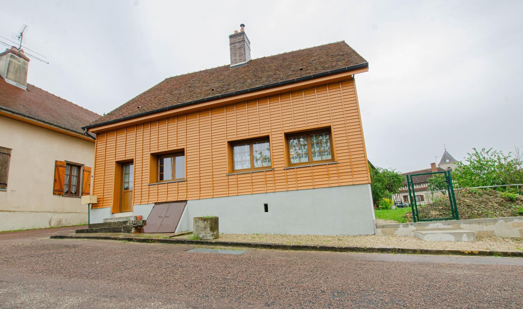 Et toetagers hus med skråtag, skorsten og en lille veranda med bænk.
