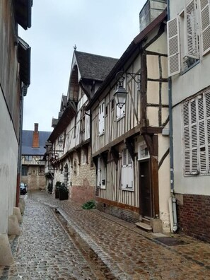 Une ruelle étroite pavée, bordée de bâtiments traditionnels à colombages, un ciel dégagé et une voiture garée.