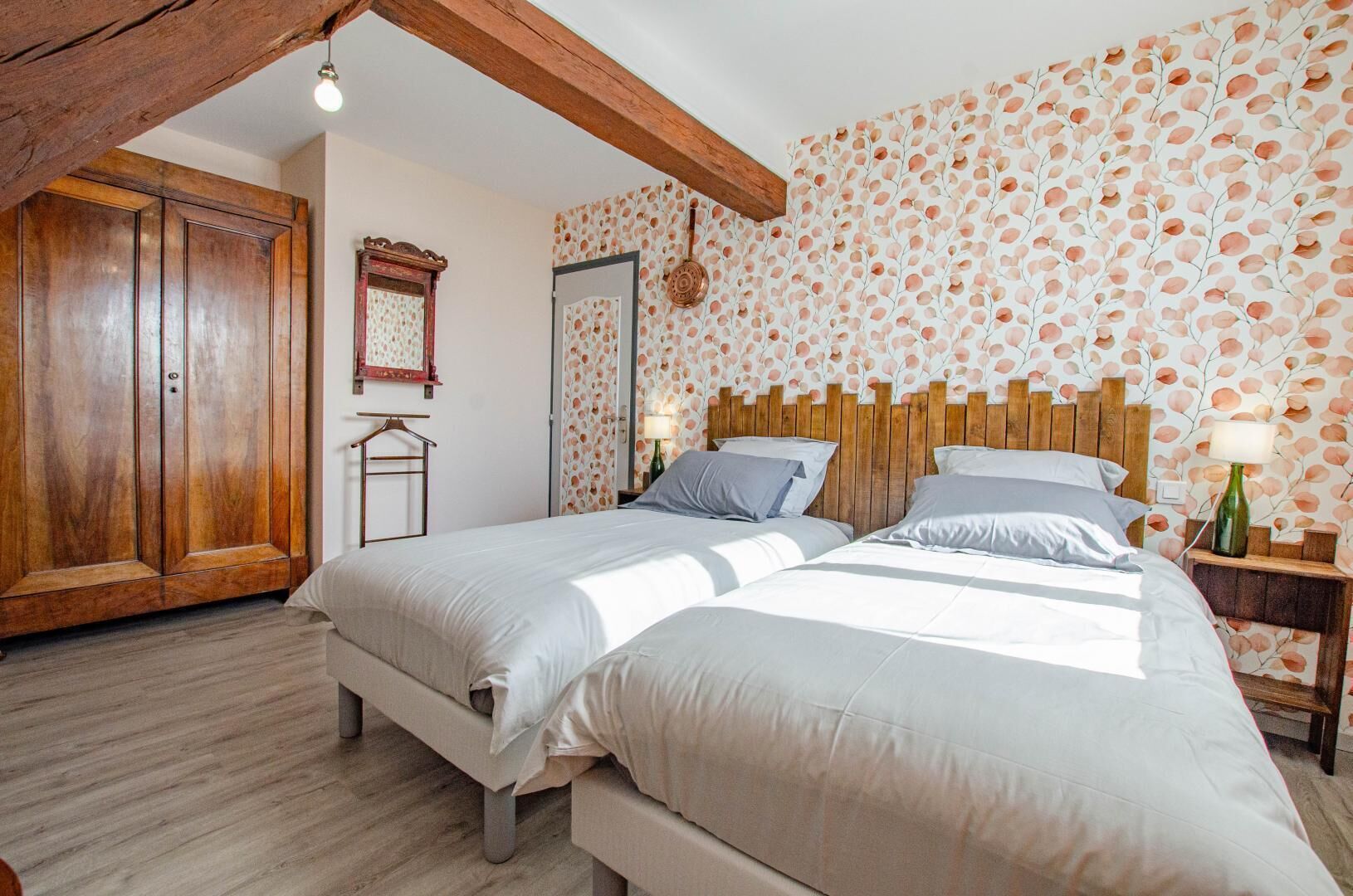 A bedroom with two beds, wooden headboard, a wardrobe, and a wall with a leaf pattern.