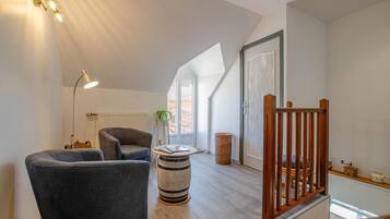Ein modernes Loft mit hohen Decken, einer Holztreppe und einer gemütlichen Sitzecke mit einem runden Tisch und zwei Sesseln.
