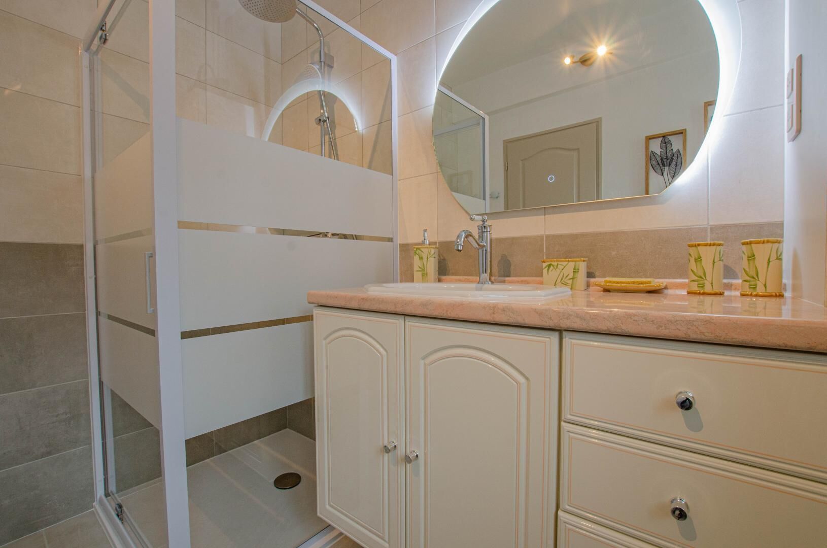 Un baño moderno con cabina de ducha de vidrio, un espejo grande y un lavamanos con cajones para guardar objetos.