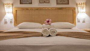 Een net opgemaakt bed met opgerolde handdoeken en een decoratief kussen, twee wandlampen en drie ingelijste kunstwerken aan de muur.