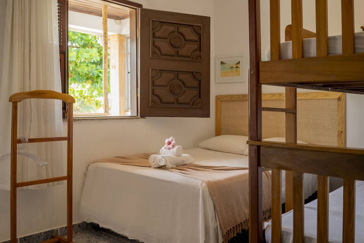 Ein Schlafzimmer mit einem Bett, einem Holzstuhl, einem Fenster mit Vorhängen und einem Schlafplatz.