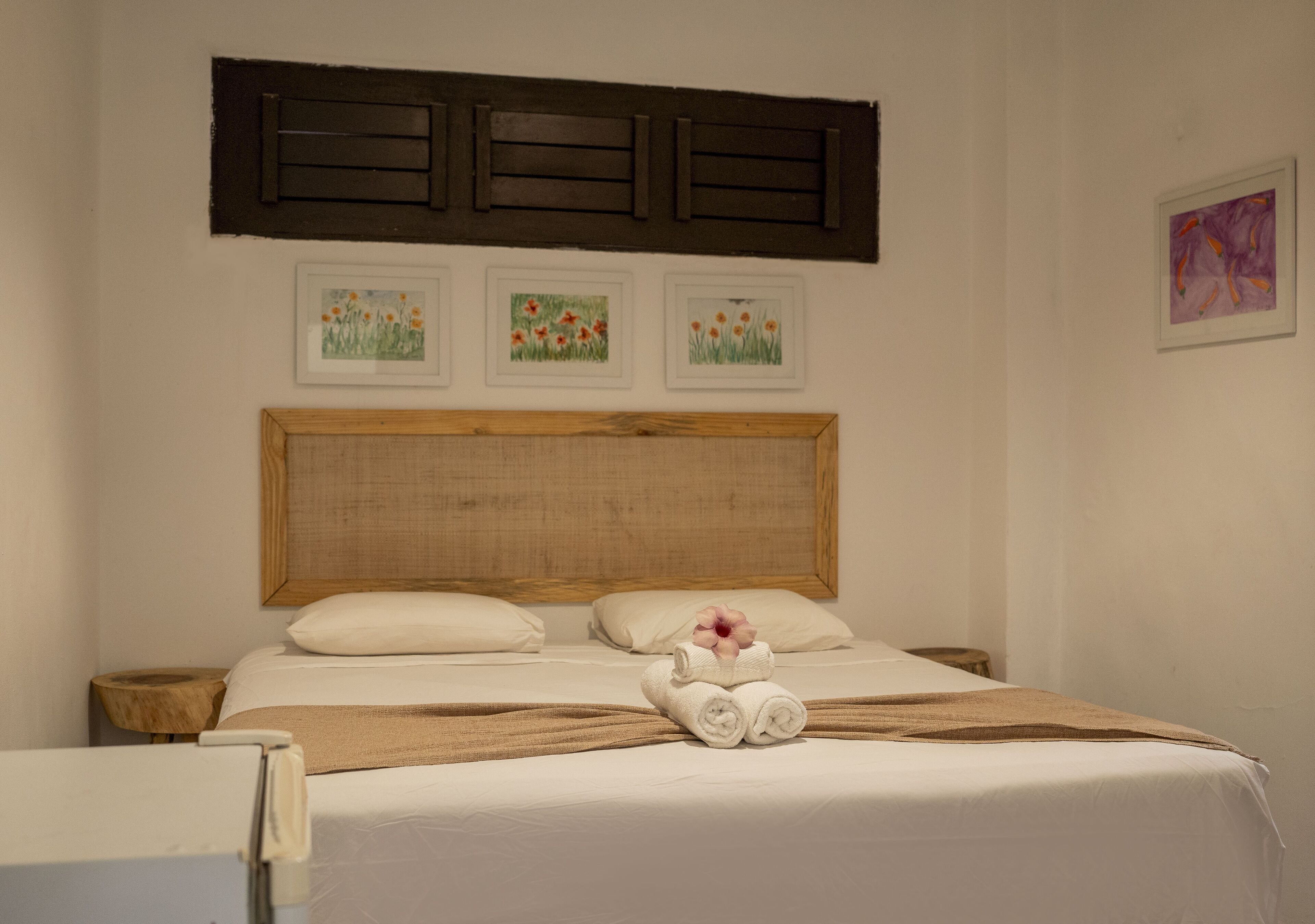 A neatly made bed with a wooden headboard, a pair of nightstands, and three framed floral paintings on the wall.