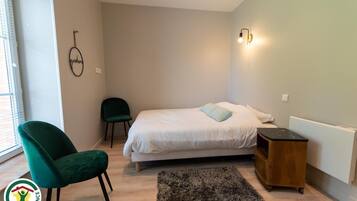 A bedroom with a bed, a green chair, a small wooden nightstand, and a wall-mounted light fixture.