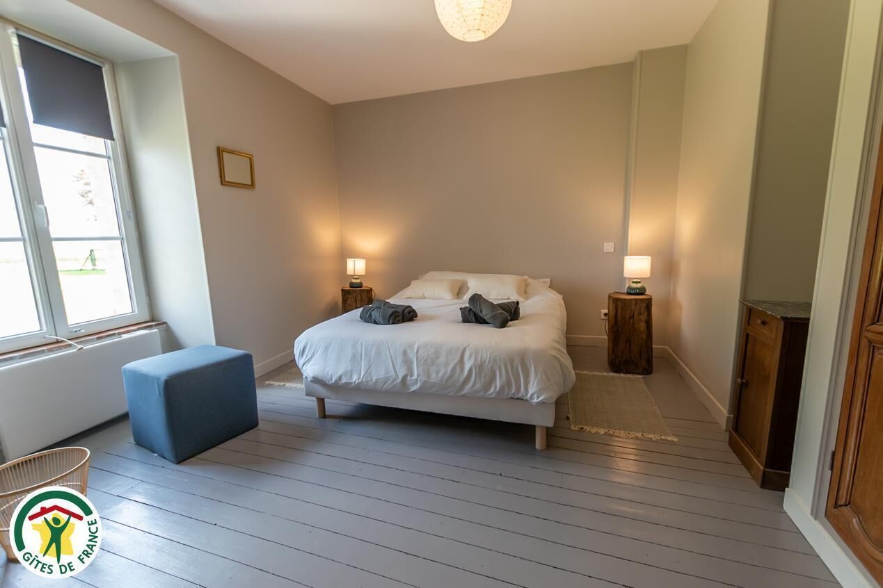 Een slaapkamer met een bed, nachtlampjes, een klein krukje en een raam met jaloezieën.
