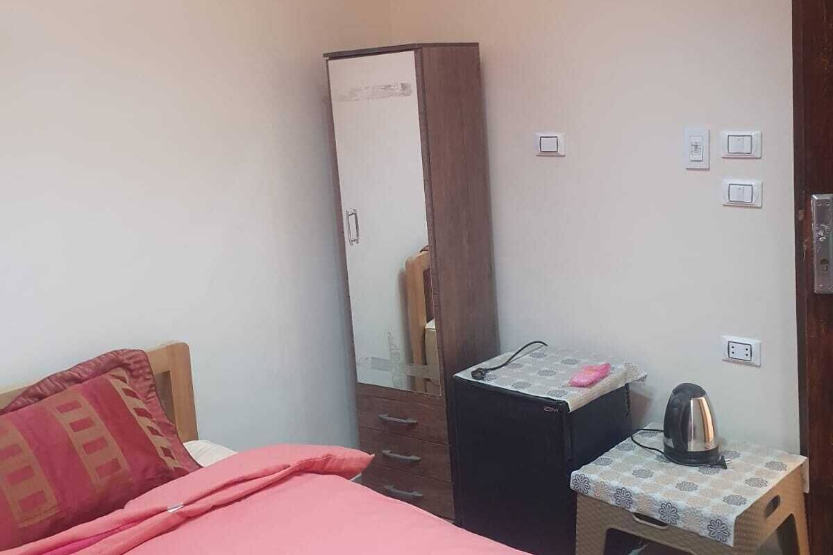 Une chambre comprenant un lit, une armoire, un climatiseur, une petite table avec une bouilloire et une prise de courant.