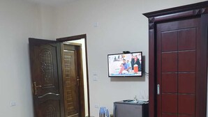 A room with a bed, a television mounted on the wall, a refrigerator, and a wooden wardrobe. - Andy guest house  (Giza)