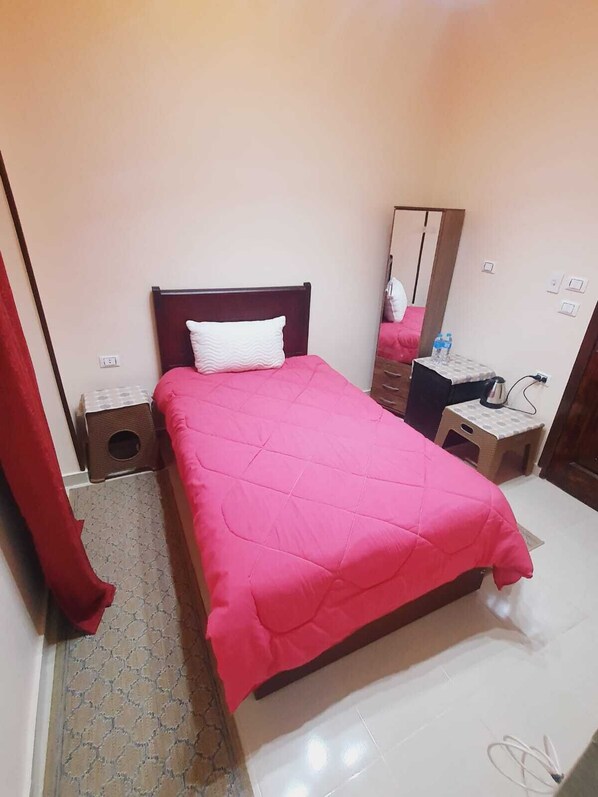 A bedroom with a bed, a mirror, a nightstand, a dresser, and a small table with a kettle. - Andy guest house (Giza)
