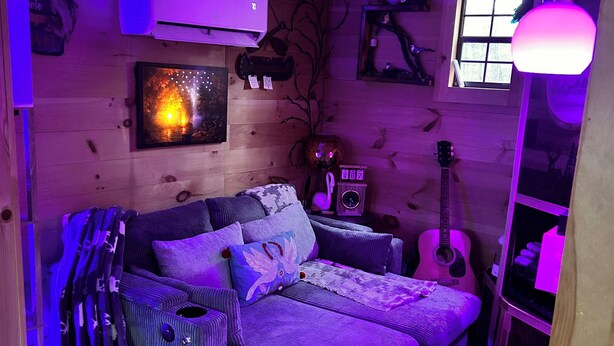 Une pièce chaleureuse avec un décor en bois, un canapé, une guitare et un radiateur fixé au mur.