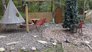Une pergola en bois avec un fauteuil suspendu, une petite table et un sapin de Noël, le tout installé dans une zone boisée.
