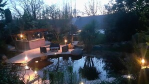 Un espacio exterior tranquilo con un estanque, asientos e iluminación ambiental.