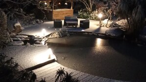 Un espacio al aire libre iluminado por la noche, con un pabellón de madera, asientos y una pequeña fuente de agua.