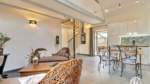 Una sala de estar moderna con un sofá, una mesa de comedor con sillas, una escalera y una zona de cocina.