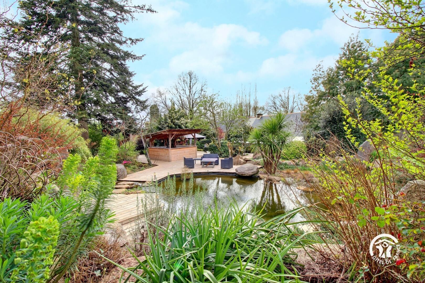 Un jardin paisible avec une terrasse en bois, un petit étang et un kiosque.