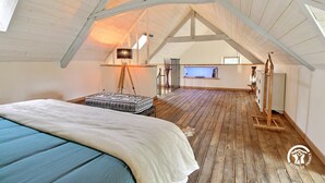 Un espacioso dormitorio en el ático con suelo de madera, una cama, un escritorio y un ventanal grande.