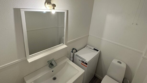 Un baño pequeño y limpio con lavamanos, espejo y retrete blancos.