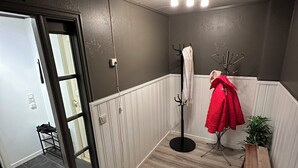A room with a wooden floor, a coat rack with a red jacket, a bench, and a door leading to another room.