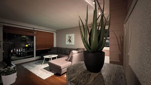 Una sala de estar moderna con un sofá gris, una mesita blanca pequeña y una gran planta de aloe vera en maceta.