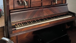 A grand piano in a room with wooden paneling on the ceiling and a window with blinds.