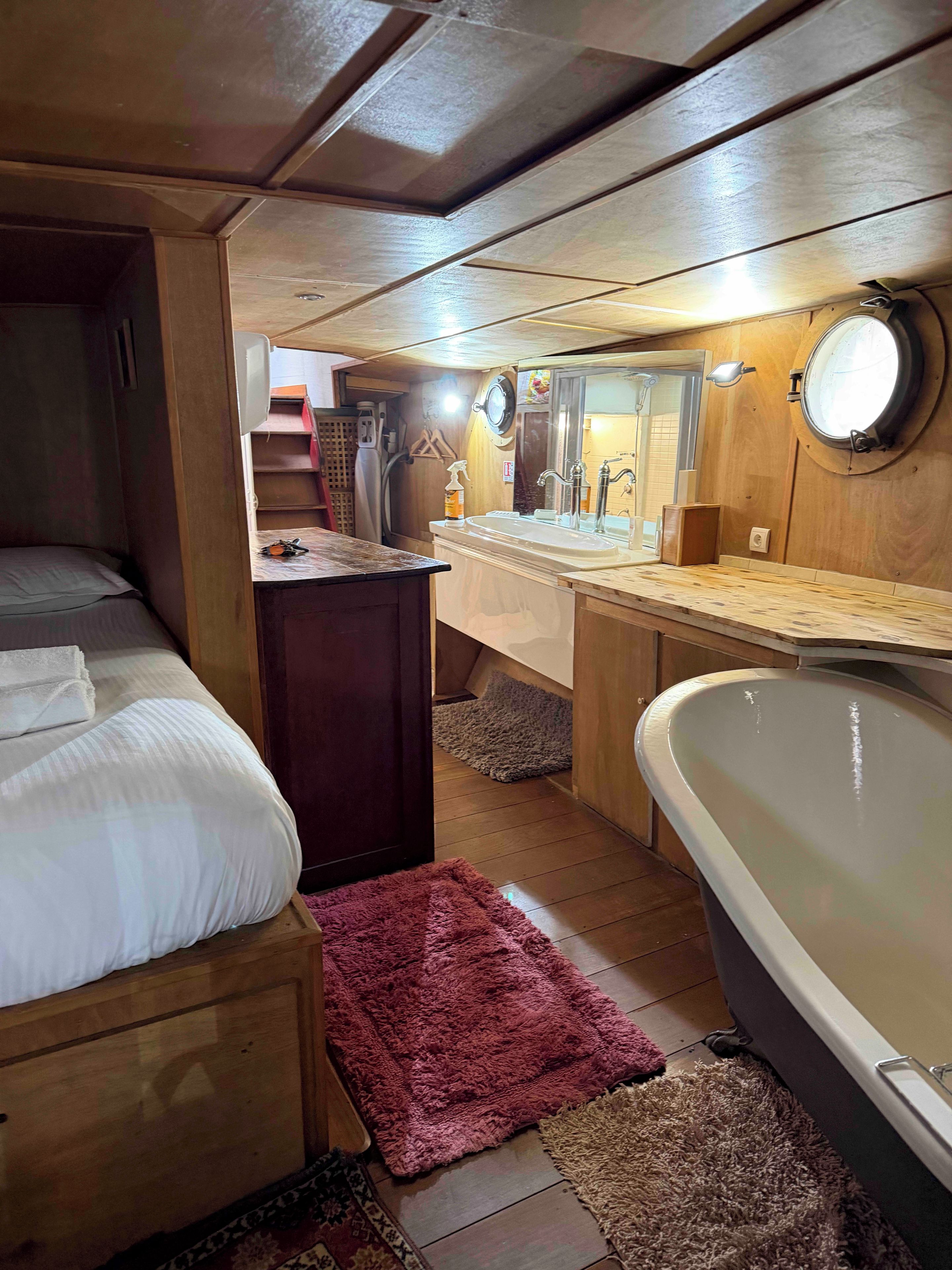 Een compacte kamer in chaletstijl met een bed, een klein bureau, een wastafel en een bad.