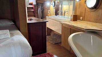 Een compacte kamer in chaletstijl met een bed, een klein bureau, een wastafel en een bad.