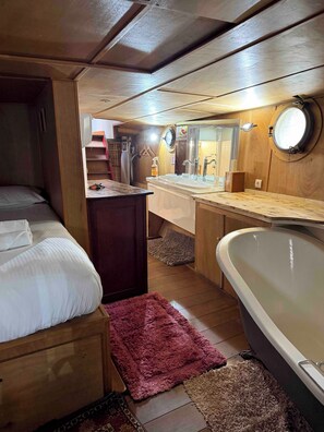 A compact, cabin-style room with a bed, a small desk, a sink, and a bathtub.