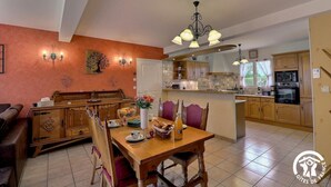 Una cocina amplia con armarios de madera, un comedor con mesa y sillas de madera, y una araña.