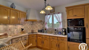 Una cocina con armarios de madera, microondas, horno y una ventana con cortinas.