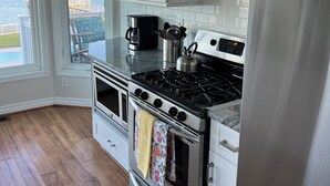 A kitchen with white cabinets, stainless steel appliances, and a view of a body of water through a sliding glass door. - Waterway Home with Private Dock, Private Pool and Fenced in yard (Ocean Isle Beach)