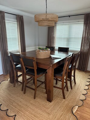 A dining area with a wooden table, chairs, a woven basket, and a hanging light fixture. - Waterway Home with Private Dock, Private Pool and Fenced in yard (Ocean Isle Beach)