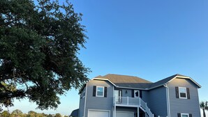 A two-story house with a garage, a covered porch, and a staircase leading to the second floor. - Waterway Home with Private Dock, Private Pool and Fenced in yard (Ocean Isle Beach)