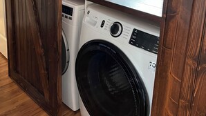 A laundry room with a washing machine and dryer, wooden flooring, and a window with blinds. - Waterway Home with Private Dock, Private Pool and Fenced in yard (Ocean Isle Beach)