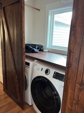 A laundry room with a washing machine and dryer, wooden flooring, and a window with blinds.