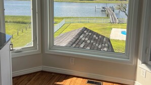 A room with two large windows offering a view of a lake, a dock, and a grassy area. - Waterway Home with Private Dock, Private Pool and Fenced in yard (Ocean Isle Beach)