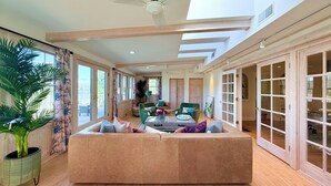 A spacious living area with a large beige sofa, a ceiling fan, and a view of the outdoors through large windows.
