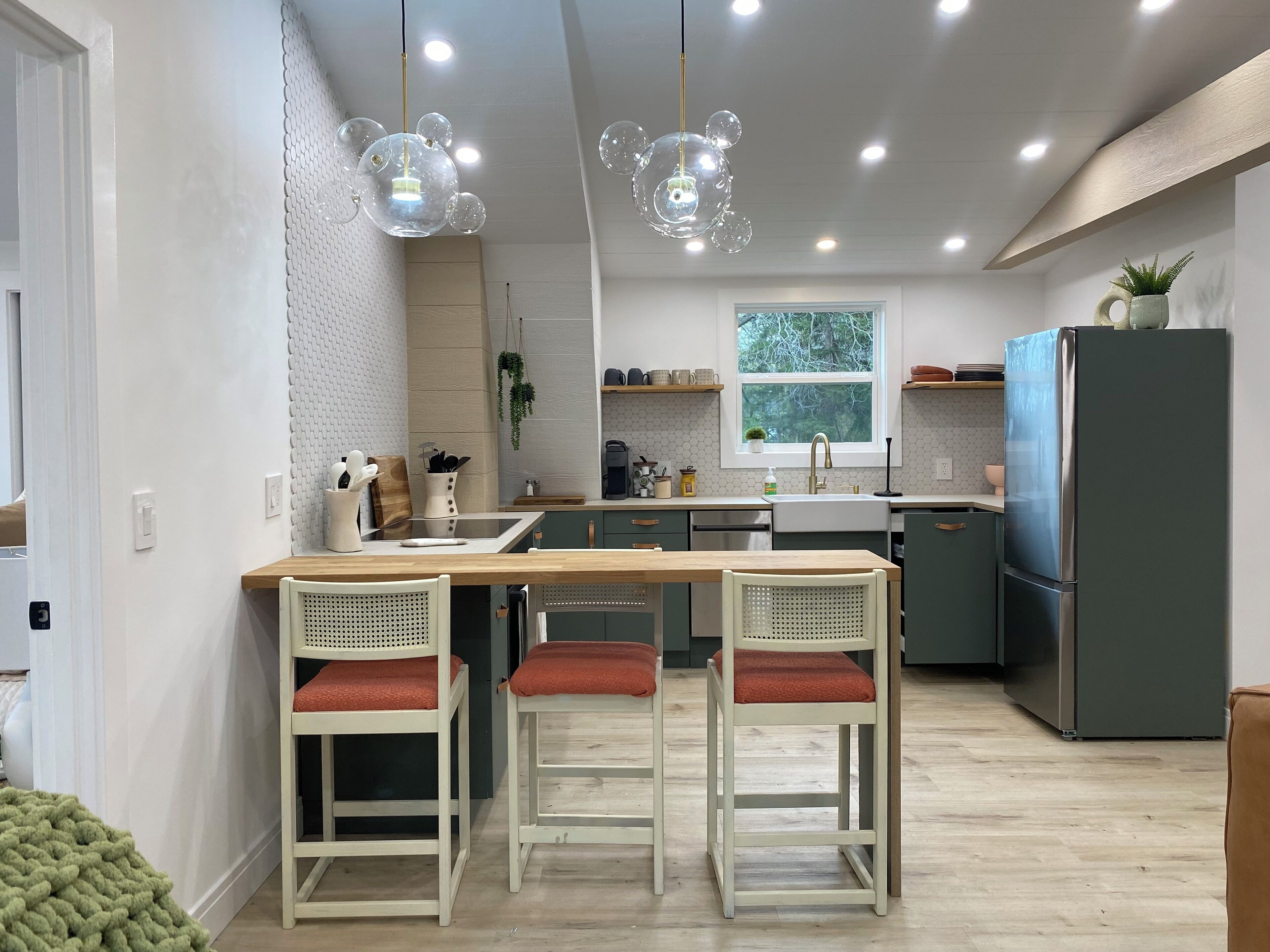 Cocina moderna con una isla central, taburetes de bar, un refrigerador e iluminación colgante.