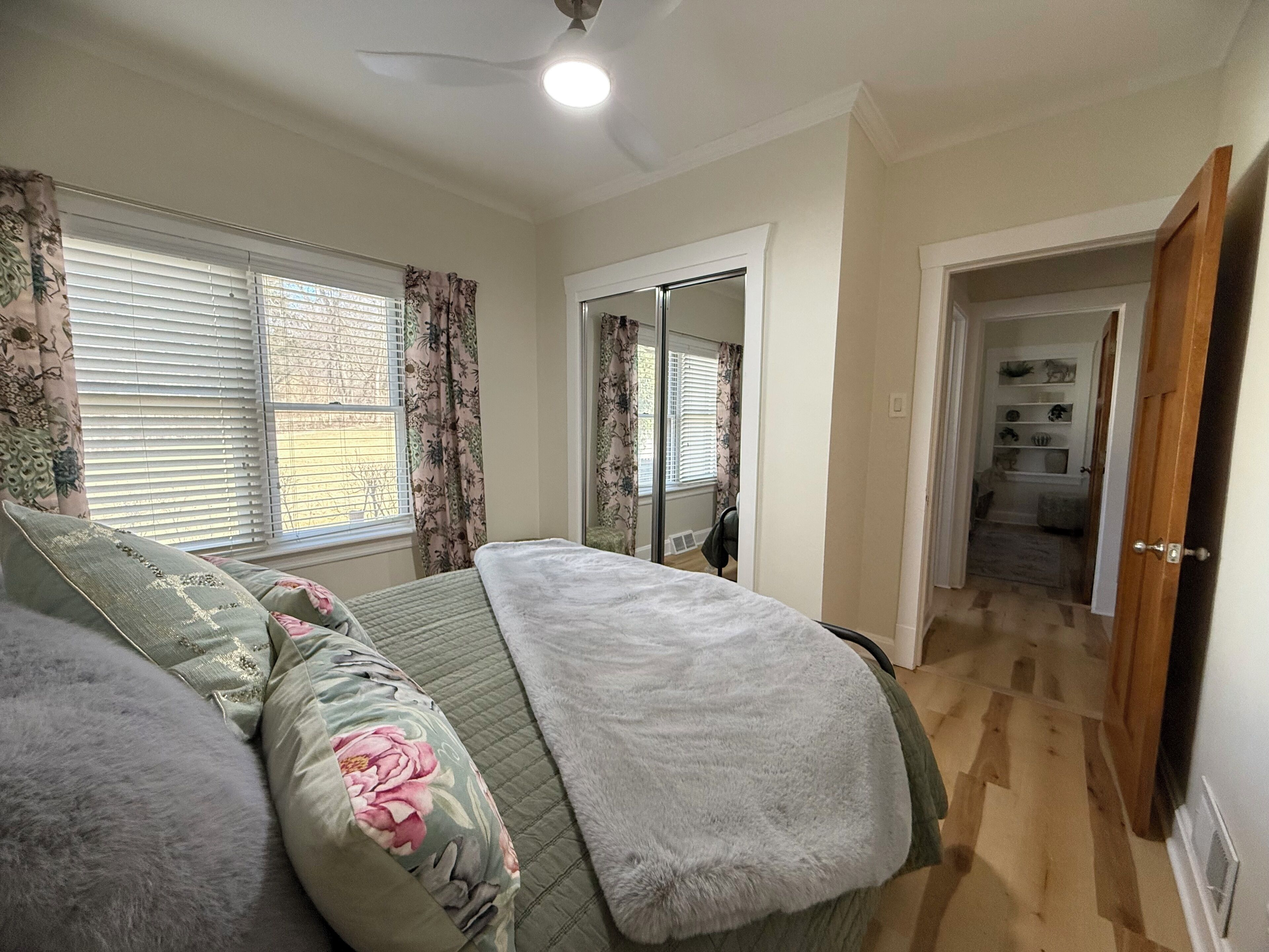 A bedroom with a bed, a ceiling fan, and a view of a hallway.