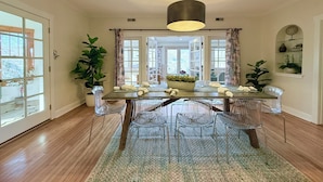 A dining area with a wooden table, clear chairs, a central plant, and a hanging light fixture.