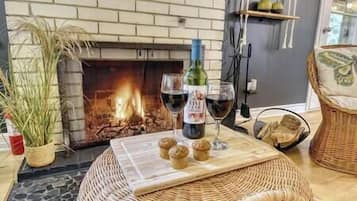 A cozy room with a fireplace, a bottle of wine, glasses, and a basket of muffins on a table.