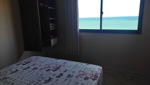 A room with a bed, a wardrobe, and a window with a view of the sea. - Edifício Flat Euro (Natal)