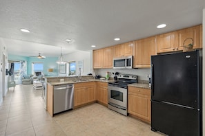 A modern kitchen with wooden cabinets, stainless steel appliances, and a tiled floor.