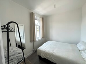 A bedroom with a single bed, a radiator, a window with curtains, and a mirror on the wall. - Cosy London Apartment by Underground Train station - Elizabeth Line + Parking (Ilford)
